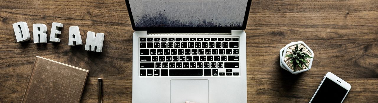 Schreibtisch mit einem Laptop, Smartphone und einem Notizbuch (Symbolbild)